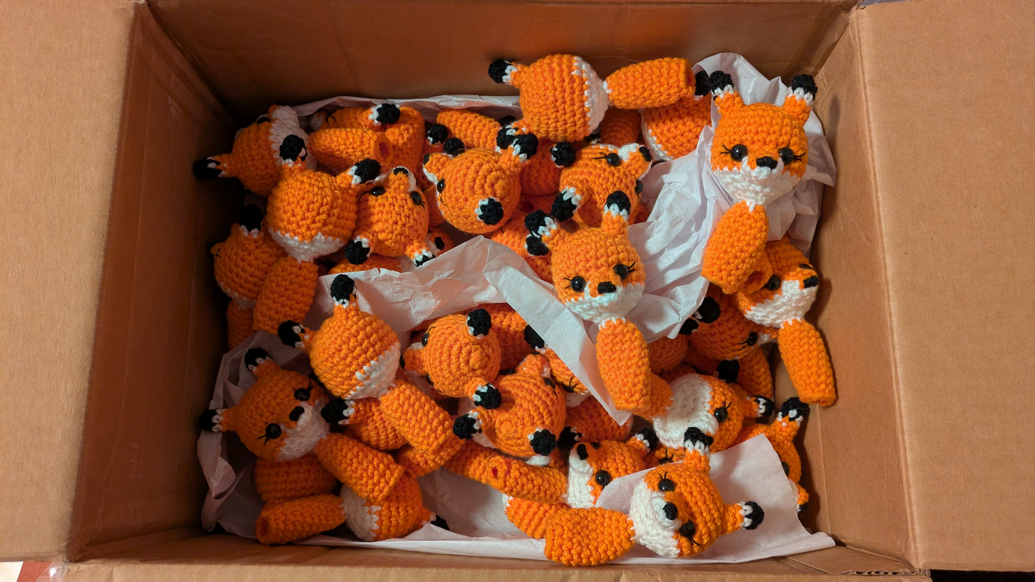 open cardboard box full of crocheted Vox Pupuli logo foxes